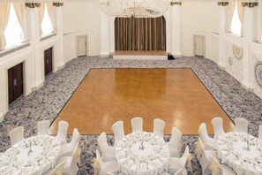 Une vaste salle de bal dotée d’une scène centrale, de chaises blanches et d’un tapis à motifs.