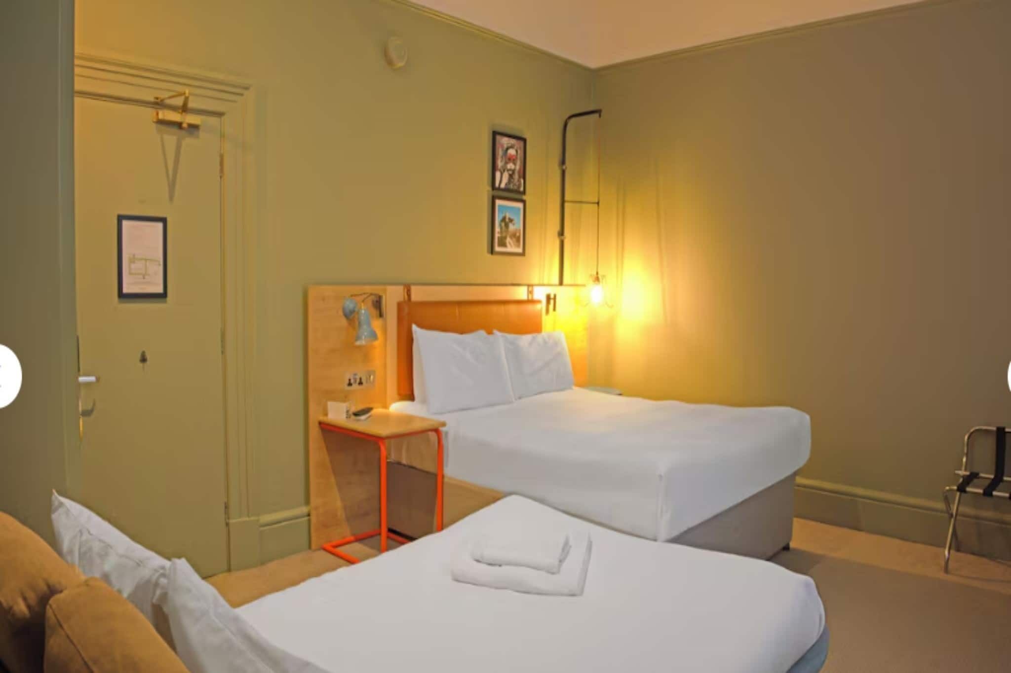 A hotel room with two beds, a wooden headboard, a small table, and a chair.