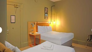 Hotellihuone, jossa on kaksi sänkyä, puinen sängynpääty, pieni pöytä ja tuoli.