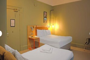 A hotel room with two beds, a wooden headboard, a small table, and a chair. - Standard Family of 3 Room (Bristol)