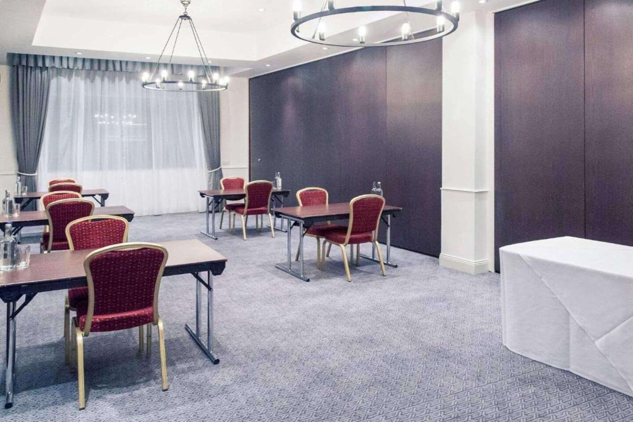 A conference room with tables and chairs, a chandelier, and a large window with curtains.