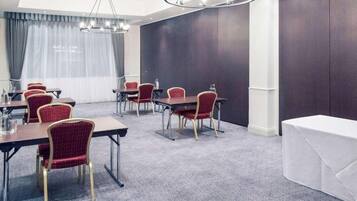 A conference room with tables and chairs, a chandelier, and a large window with curtains.