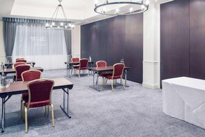 Una sala conferenze con tavoli e sedie, un lampadario e un'ampia finestra con tende.