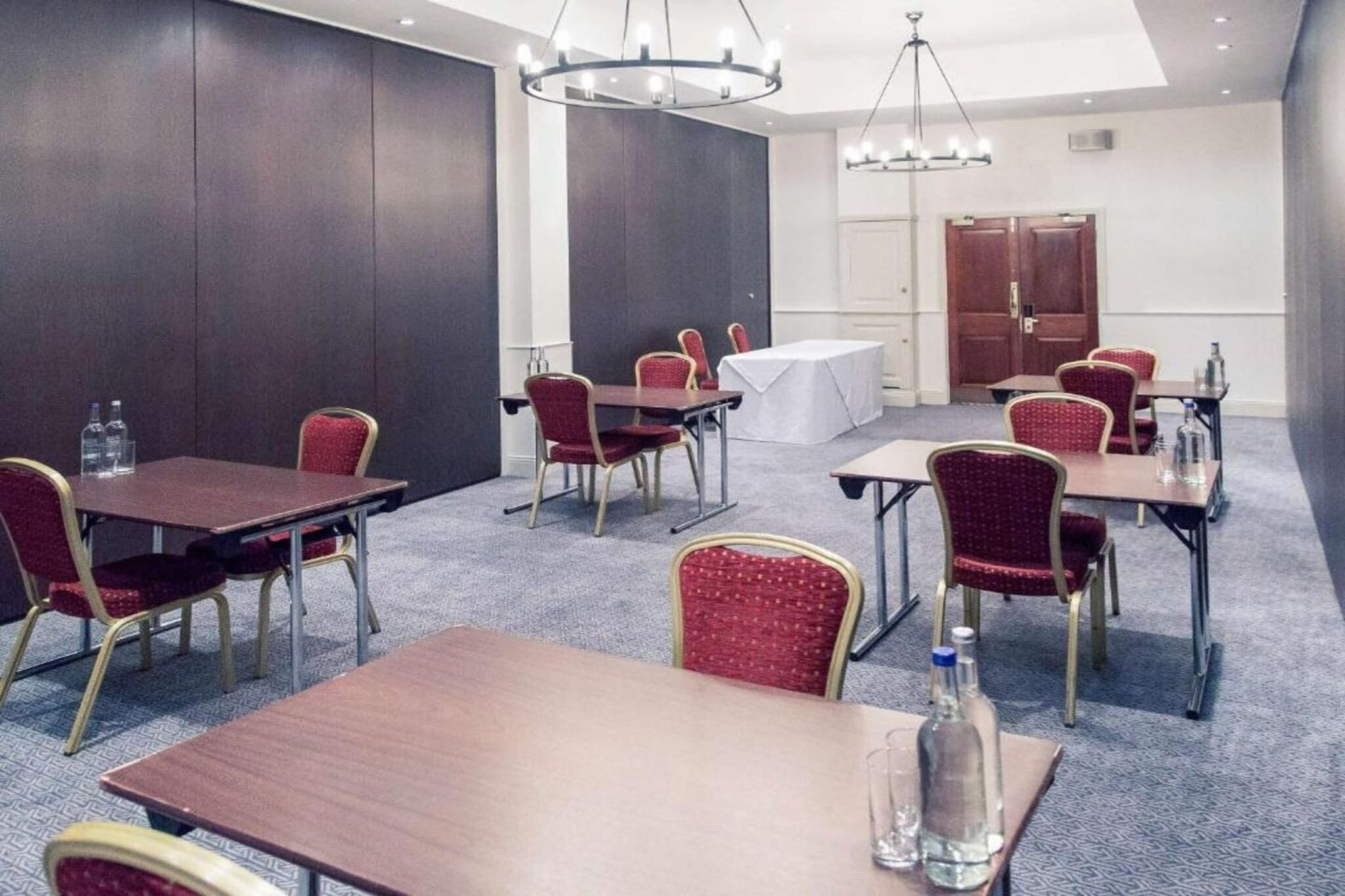 A conference room with tables and chairs, a chandelier, and a door in the background.