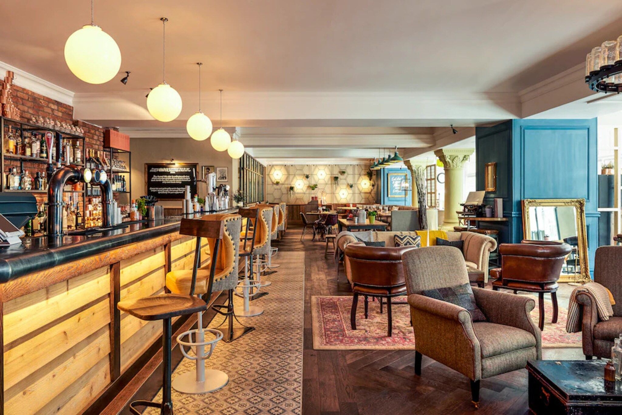 A bar area with stools, a counter, and a variety of bottles. There are multiple seating areas with chairs and a sofa.