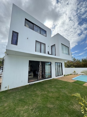 Ein modernes, zweistöckiges Haus mit großem Glasflurtür, Schwimmbad und gepflegtem Rasen.