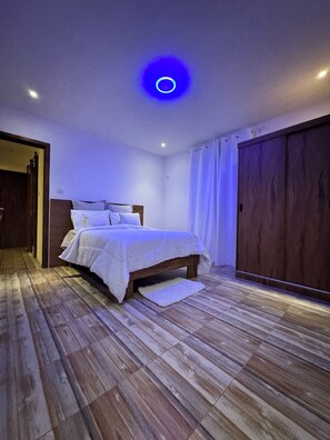 Ein Schlafzimmer mit einem hölzernen Bett, einem weißen Teppich und einer blauen Deckenleuchte.