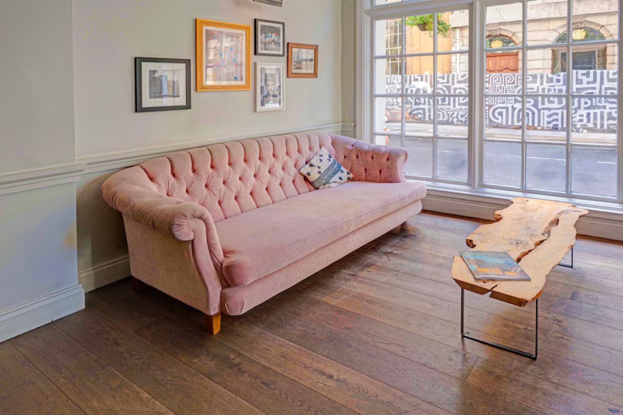 A room with a pink tufted sofa, a wooden coffee table, and framed pictures on the wall.