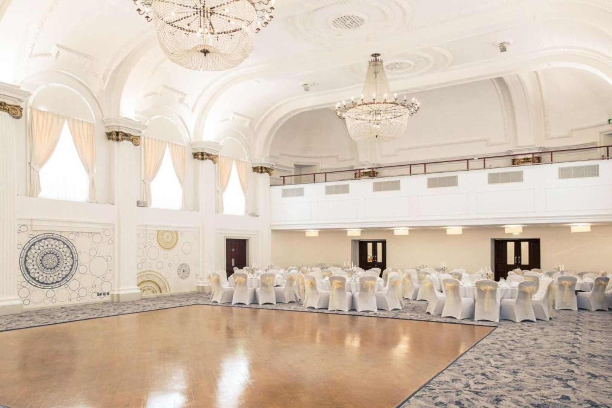 A large hall with a polished floor, white walls, and chandeliers.
