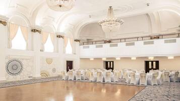 A large hall with a polished floor, white walls, and chandeliers.