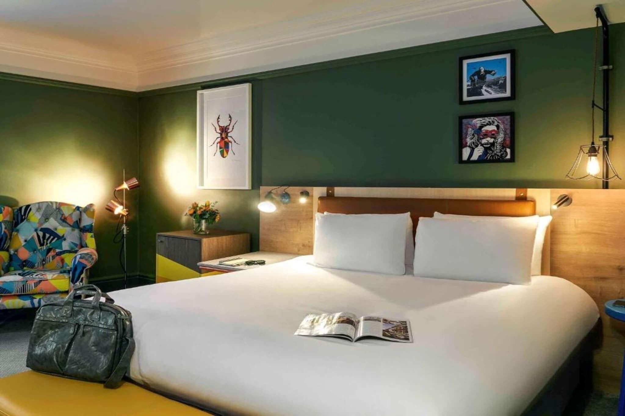 A hotel room with a bed, a nightstand, a lamp, a chair, and a suitcase.