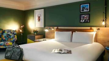 A hotel room with a bed, a nightstand, a lamp, a chair, and a suitcase.