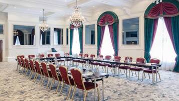 A conference room with a long table, red chairs, chandeliers, and large windows with curtains.
