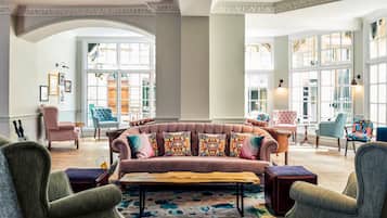 A spacious lounge area with a large, plush sofa adorned with colorful pillows, surrounded by various seating options and a patterned rug.