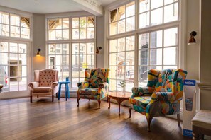 Une pièce spacieuse avec de grandes fenêtres, un fauteuil classique, des fauteuils aux couleurs vives et une petite table ronde.