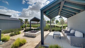 Un espace extérieur aménagé, abrité, avec un canapé et une table, un bac à plantes en béton et une structure métallique.