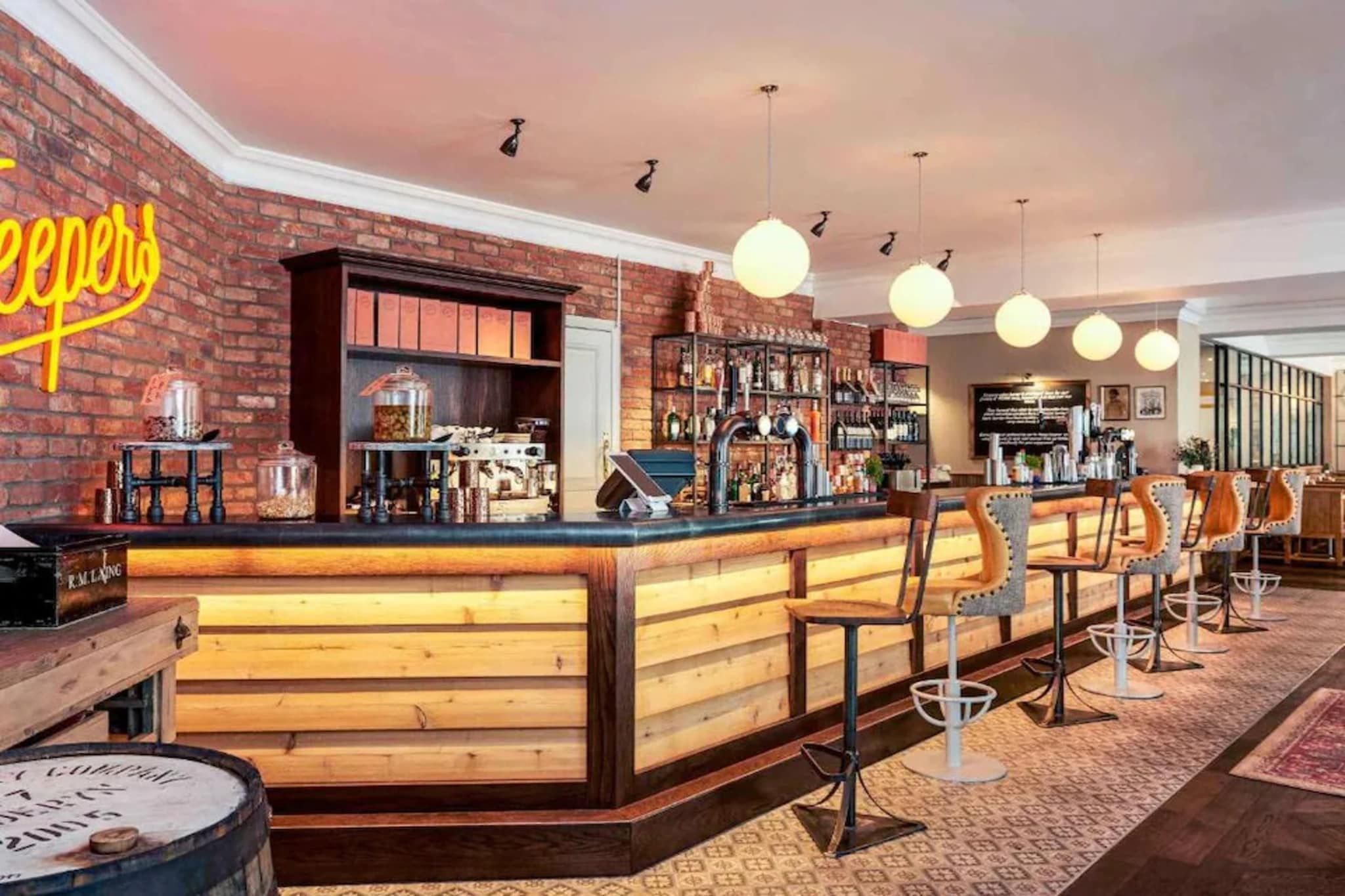 A bar area with a wooden counter, bar stools, and a brick wall.