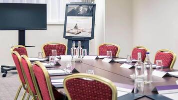 A conference room with a long table, red chairs, water bottles, and a projector screen.