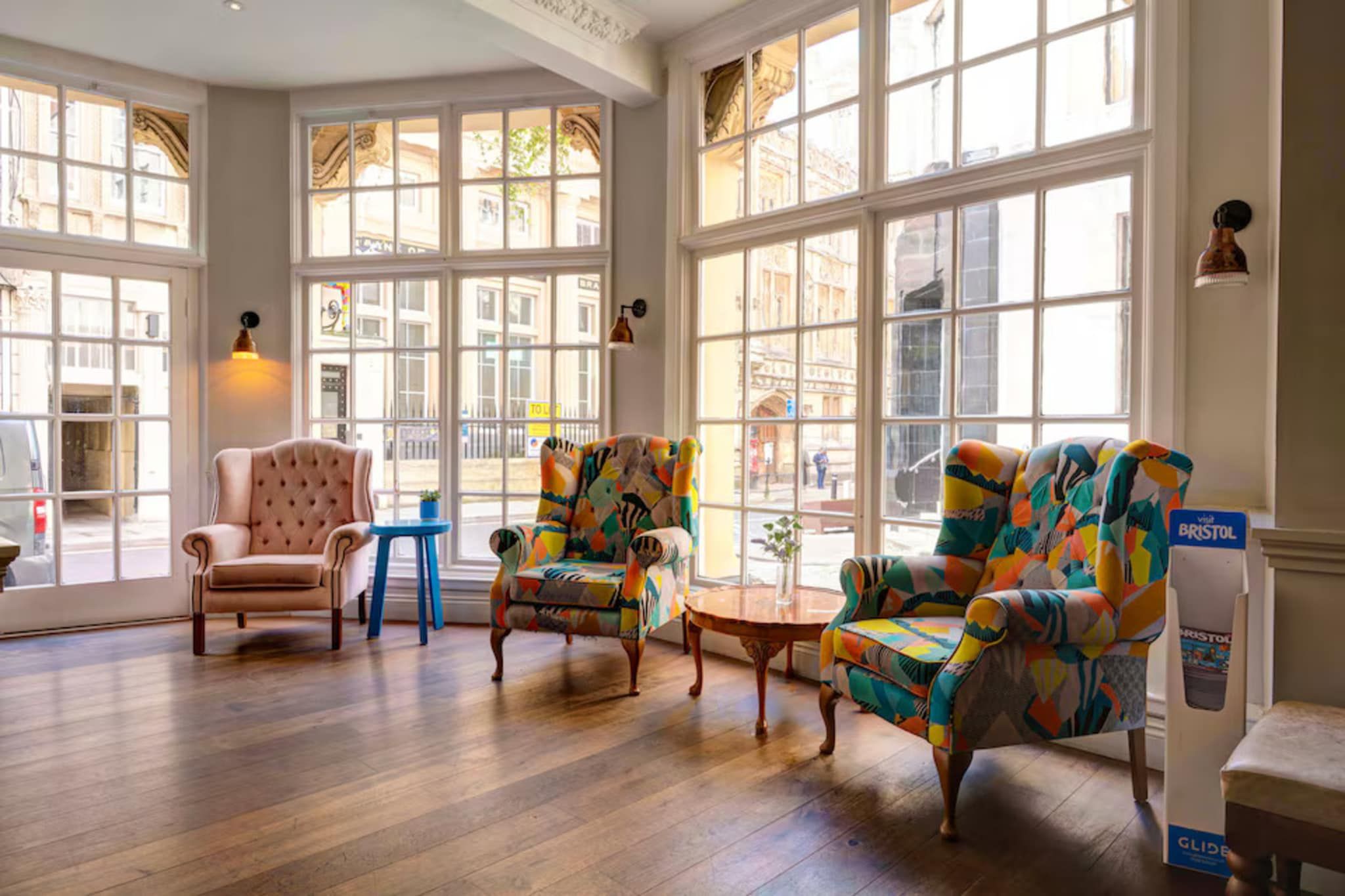 A spacious room with large windows, a classic armchair, colorful armchairs, and a small table.