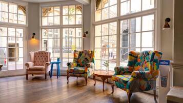 A spacious room with large windows, a classic armchair, colorful armchairs, and a small table.