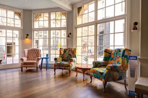 A spacious room with large windows, a classic armchair, colorful armchairs, and a small table. - Bristol Grand Hotel By Sunday - Standard Double Room (Bristol)