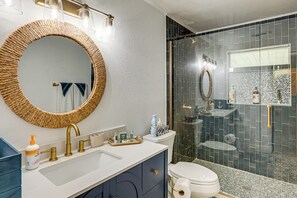 A bathroom with a round mirror, a white sink, a gold faucet, and a glass shower enclosure. - Patio & Grill: Waterfront Lake Helen Escape! (Lake Helen)