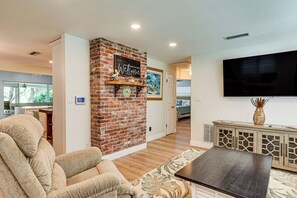 A living room with a brick accent wall, a flat-screen TV, a sofa, and a coffee table. - Patio & Grill: Waterfront Lake Helen Escape! (Lake Helen)