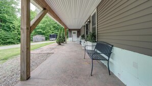 A covered porch with a bench, wooden posts, and a view of a house and greenery. - Pet Friendly Family Getaway on 15 Acres! (Gouverneur)