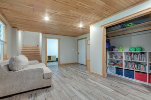 Ein Zimmer mit Holzboden, einer Couch, einem Bücherregal und einer Tür zu einem weiteren Raum.