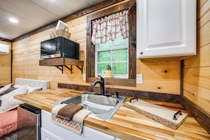 A compact kitchen with a sink, wooden countertop, and a window with curtains.