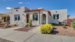Una casa moderna de dos pisos con techo de tejas rojas, un porche con escaleras y un jardín bien cuidado con diversos arbustos.