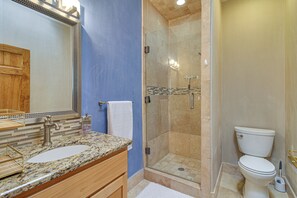 A bathroom with a granite countertop sink, a mirror, a glass-enclosed shower, and a toilet. - Walkable Home w/ Office in Downtown Albuquerque! (Albuquerque)