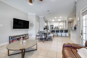 A spacious living room with a large TV, a dining area, and a kitchen in the background.