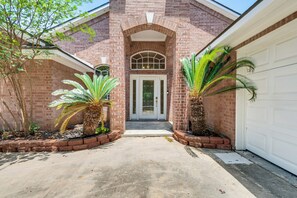 A brick building with a white garage door, a front entrance with a white door, and two palm trees in the driveway.