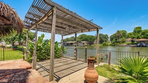 Eine Holz-Pergola mit einem Reetdach, eine große Terrakotta-Vase und Blick auf einen See mit Booten.