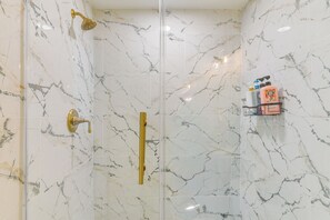 A shower with a glass door, a gold showerhead, and a marble wall. - 1 Mi to Beach & Bay! Group Getaway in Galveston (Galveston)