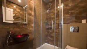 Un baño moderno con ducha envuelta en vidrio, un espejo grande y un lavabo negro tipo cuenco.