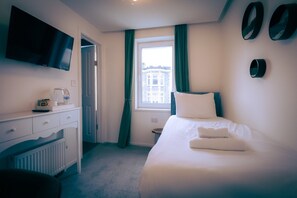 A hotel room with a bed, a desk with a television, a window with curtains, and a radiator. - Standard Single Room (Newquay)