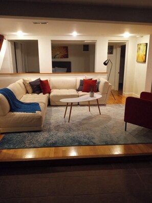 Un salon avec un canapé, une table basse et un fauteuil rouge. Il y a un tableau au mur et une lampe.