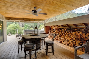 A covered outdoor area with a wooden ceiling, a table with chairs, and a stack of firewood. - Pool & Dual Decks! Modern Trinity River Retreat (Lewiston)