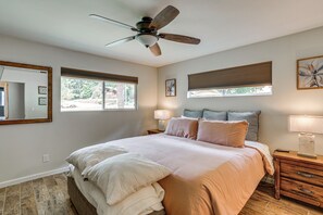 Un dormitorio con cama, ventilador de techo, mesita de noche, lámpara y ventana con persianas.