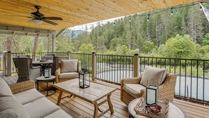 Eine überdachte Terrasse im Freien mit Rattanmöbeln, einem Deckenventilator und Blick auf ein bewaldetes Gebiet.