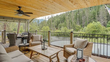 Une terrasse extérieure couverte, aménagée avec des meubles en osier, un ventilateur de plafond et offrant une vue sur une zone boisée.