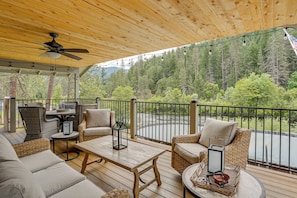 A covered outdoor seating area with wicker furniture, a ceiling fan, and a view of a forested area. - Pool & Dual Decks! Modern Trinity River Retreat (Lewiston)