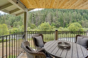 A covered outdoor seating area with wicker furniture and a round table, overlooking a forested landscape.
