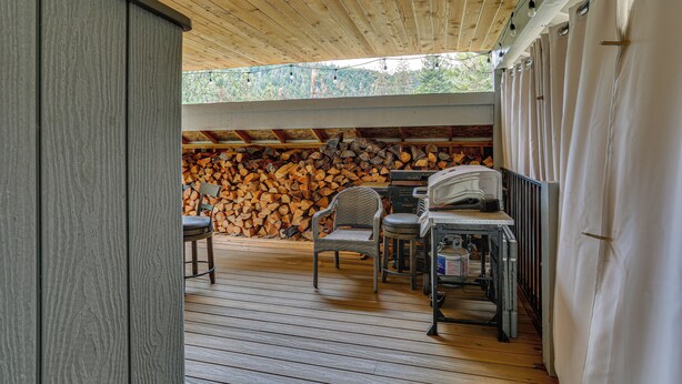 Eine überdachte Terrasse mit Holzboden, einem Stuhl, einem Tisch und einem Holzstoß.