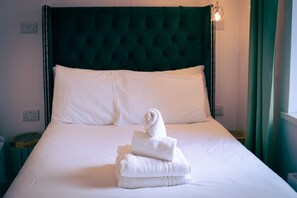 A neatly made bed with white linens and a rolled towel on top, a green upholstered headboard, and a bedside lamp. - Executive Double with Balcony & Sea View (Newquay)