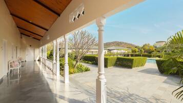 A covered outdoor area with a wooden ceiling, white columns, and a view of a landscaped garden with a pool.