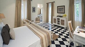 A hotel room with a bed, a desk, a chair, a dresser, and a checkered floor. - Tree of Life Sariska Manor (Rajgarh)