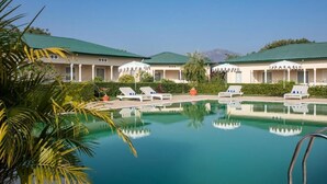 A resort with a swimming pool, lounge chairs, and a mountain view. - Tree of Life Sariska Manor (Rajgarh)